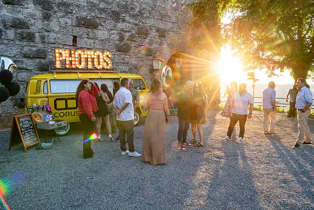The yellow photo bus with its PHOTOS sign in front of the castle wall, the evening sun bursting through the trees at the castle gate.